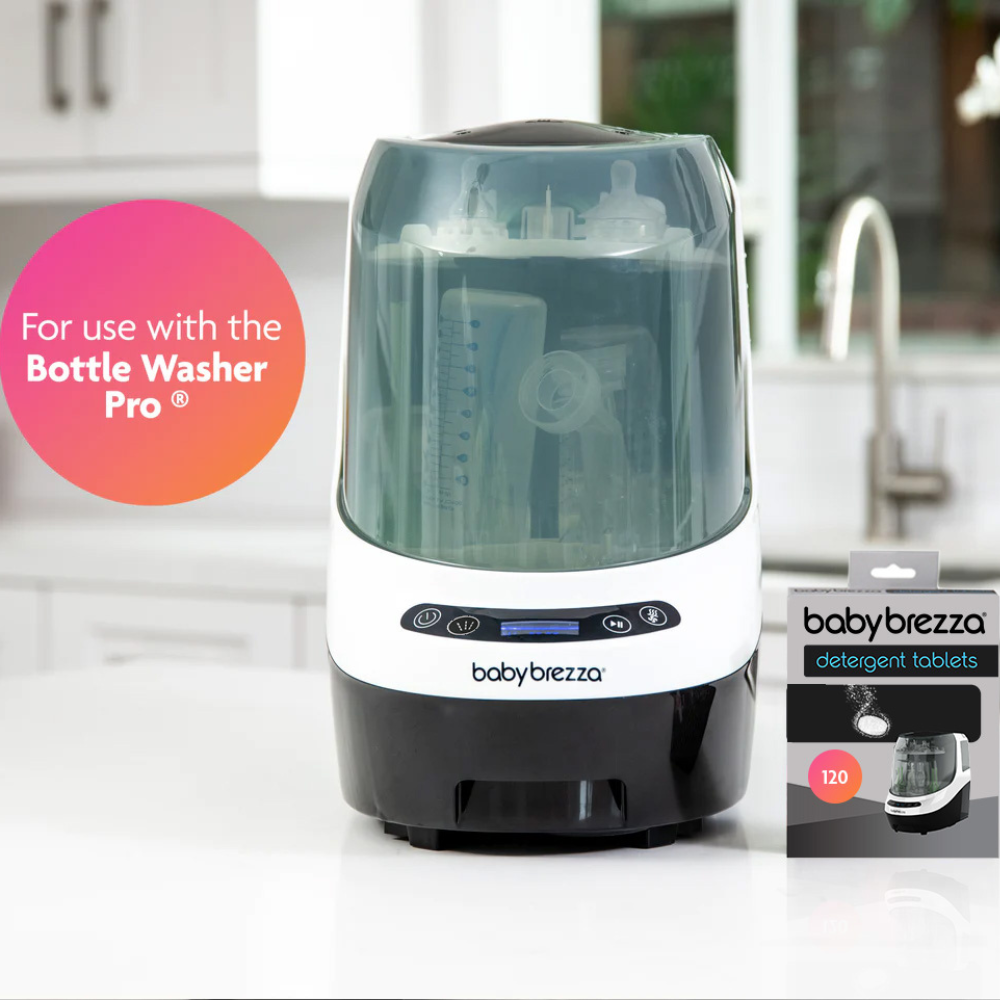 Električni čistilec za otroške stekleničke in škatlica detergentnih tablet znamke Baby Brezza stojita na beli kuhinjski površini.