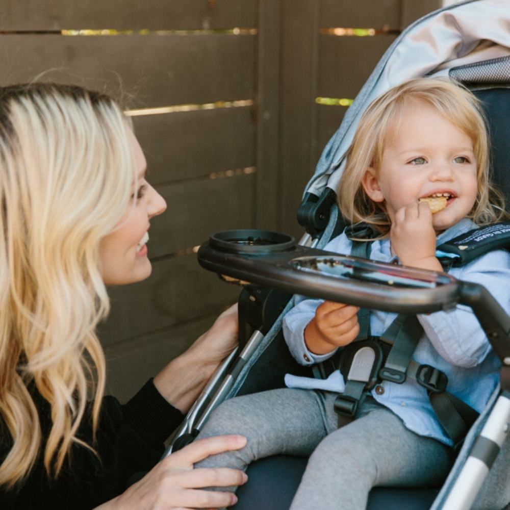 Otrok sedi na vozičku in se hrani s pomočjo mizice za hranjenje.